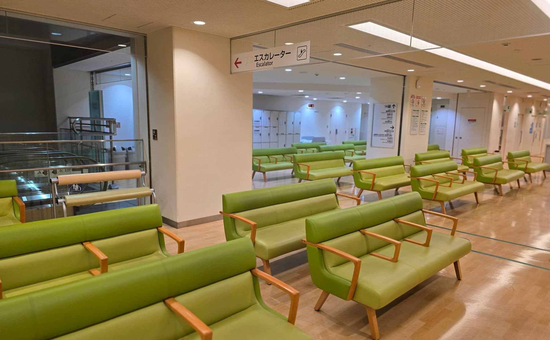 An empty hospital waiting area in Tokyo with rows of green chairs and Japanese and English signage